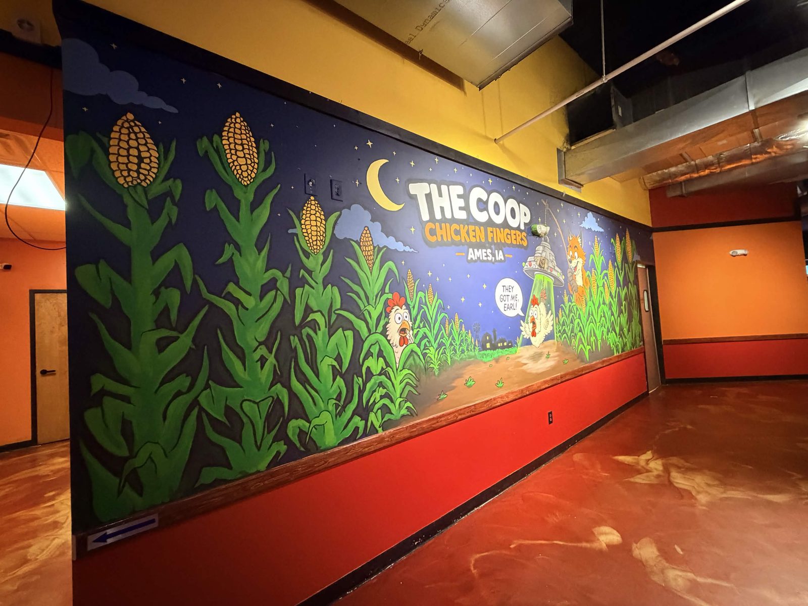 The Coop Chicken Fingers mural wall seen from the far end of the room