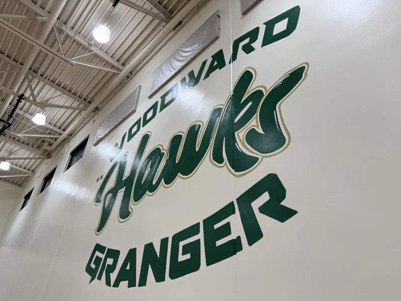 The Woodward Granger Hawks mural seen from the right side of the gym, with the hanging gym lights above it