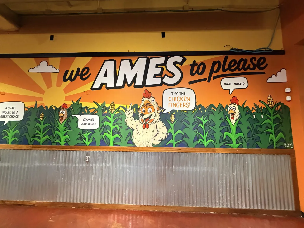 The right section of the second Coop wall painted with We Ames to Please over a rising sun, cartoon chickens and the artist signature