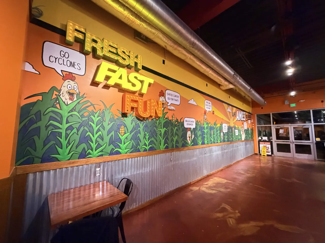The second Coop Chicken Fingers mural seen from the left end of the dining room, with FRESH, FAST and FUN letters and chickens among the corn