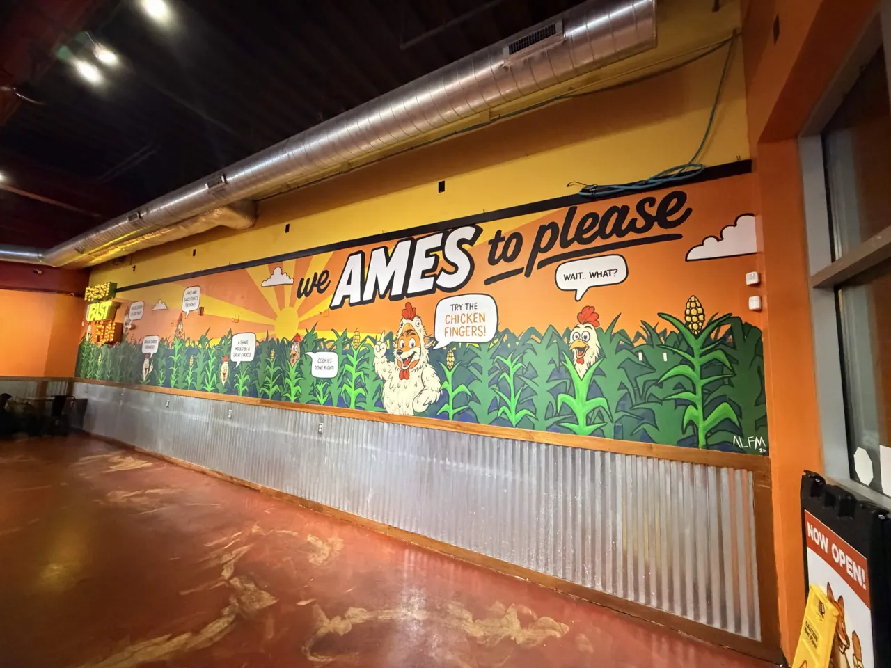 The second Coop Chicken Fingers mural seen from the right end of the dining room, with the We Ames to Please lettering and artist signature