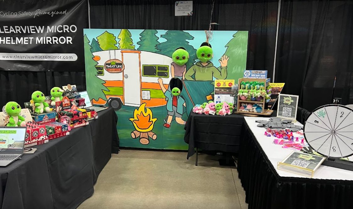 The Timberline Campground painted photo stand-in board on display at a vendor booth, with plush turtles set in the face cutouts