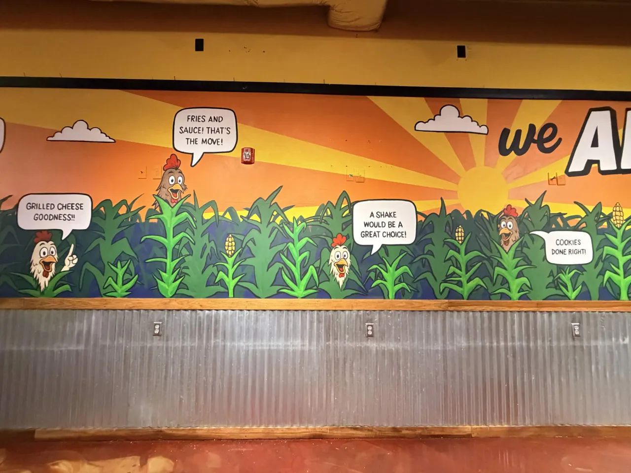 Detail of the second Coop wall: cartoon chickens popping up among green cornstalks against a sunrise sky