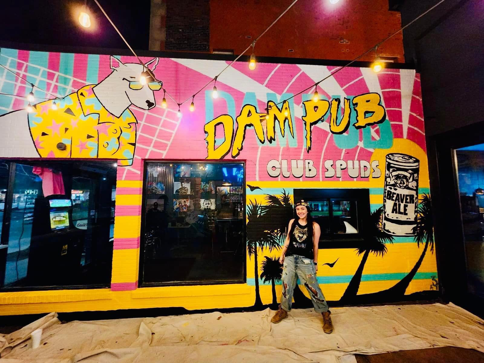 Amanda Fatino standing in front of the Dam Pub mural at night